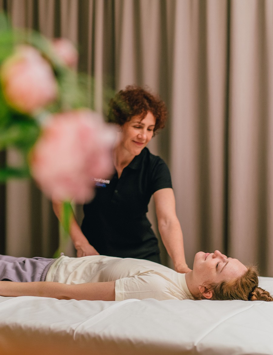 Hotel Reiters Supreme - Dame entspannt auf Liege, Therapeutin daneben behandelt den Arm